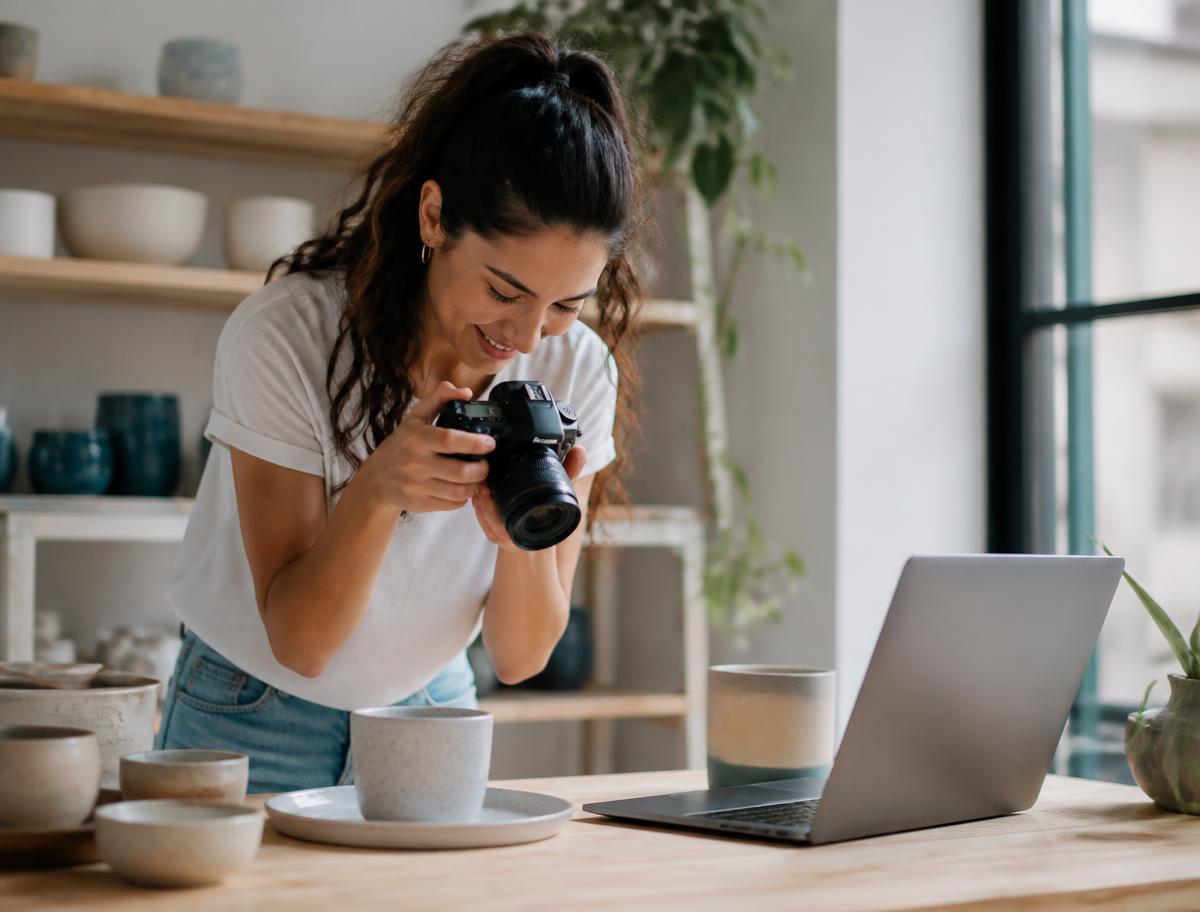 Creative business owner photographing handmade ceramics beside her laptop